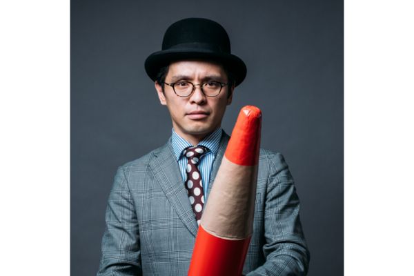 ポーラーハットにメガネをかけてスーツを着た男性と大きな赤鉛筆