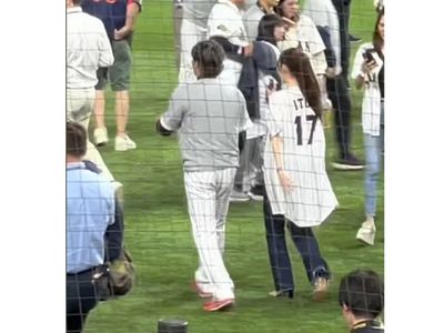 野球グラウンドを歩く選手とユニホームを羽織ったポニーテールの女性