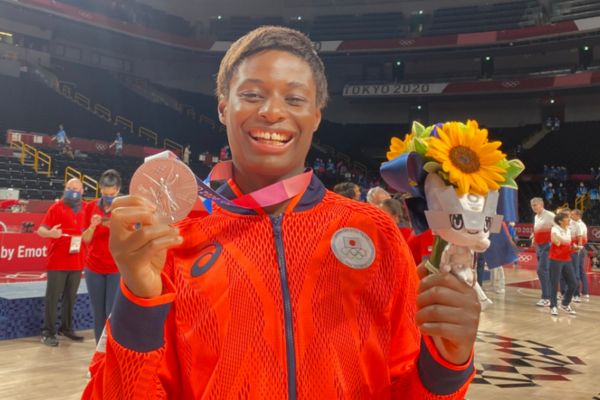 右手に金メダル、左手にひまわりの花束を持つ黒人の女性のバスケットボール選手
